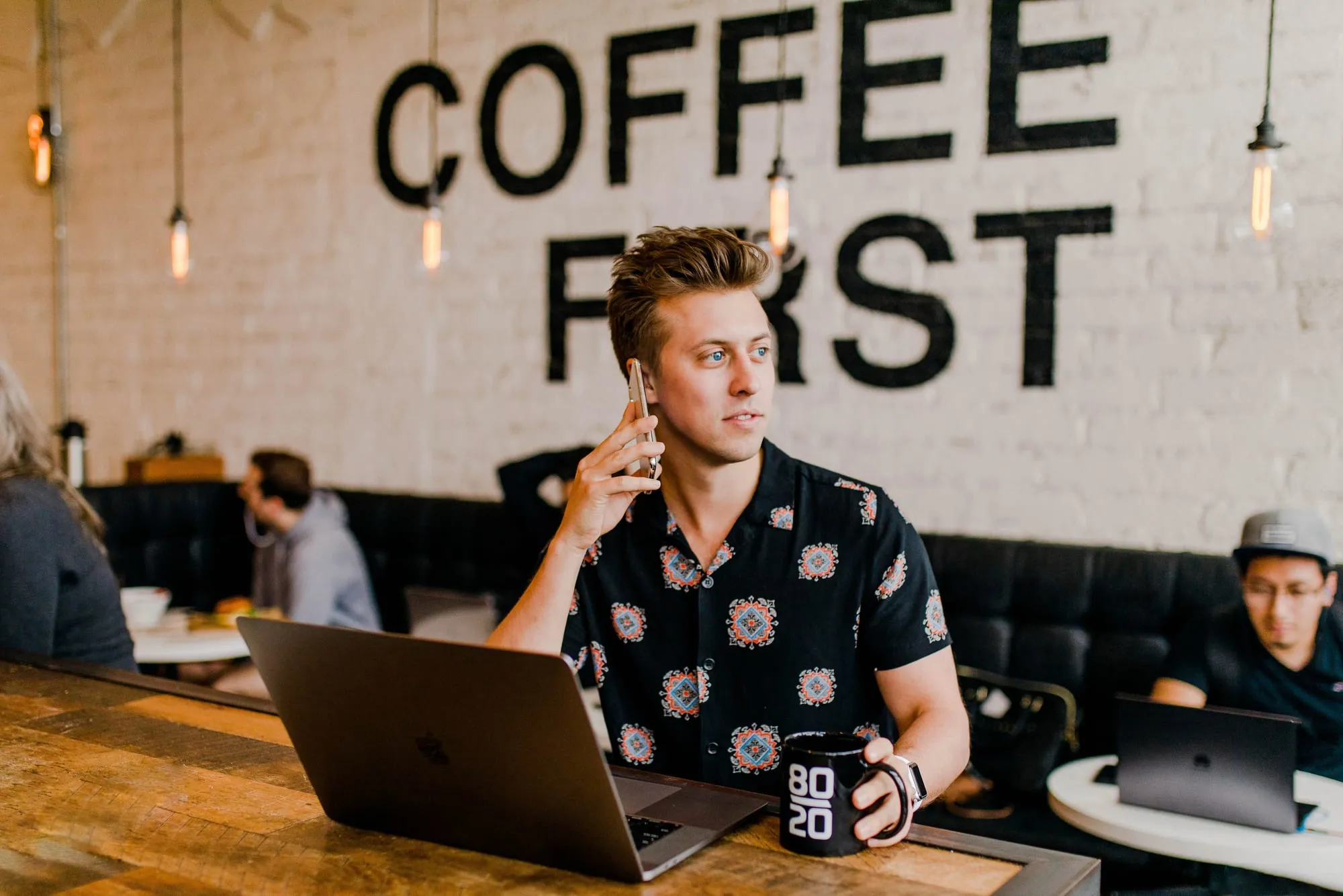 Een maker belt met een opdrachtgever, achter zijn laptop in een koffiebar